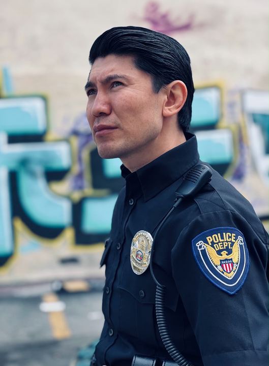 Profile of Medet in police uniform against a mural